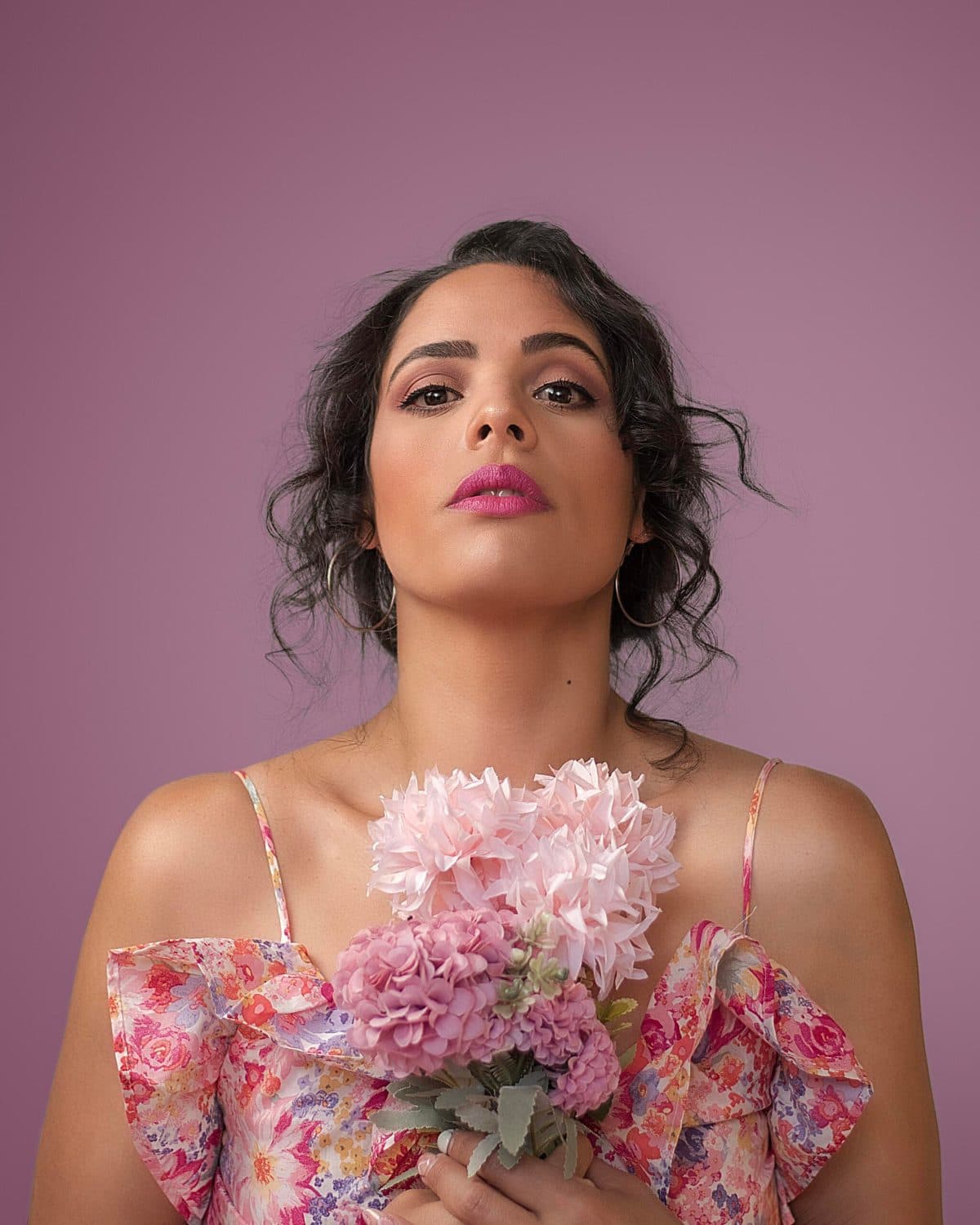 Retrato editorial sosteniendo un ramo de flores sobre fondo malva