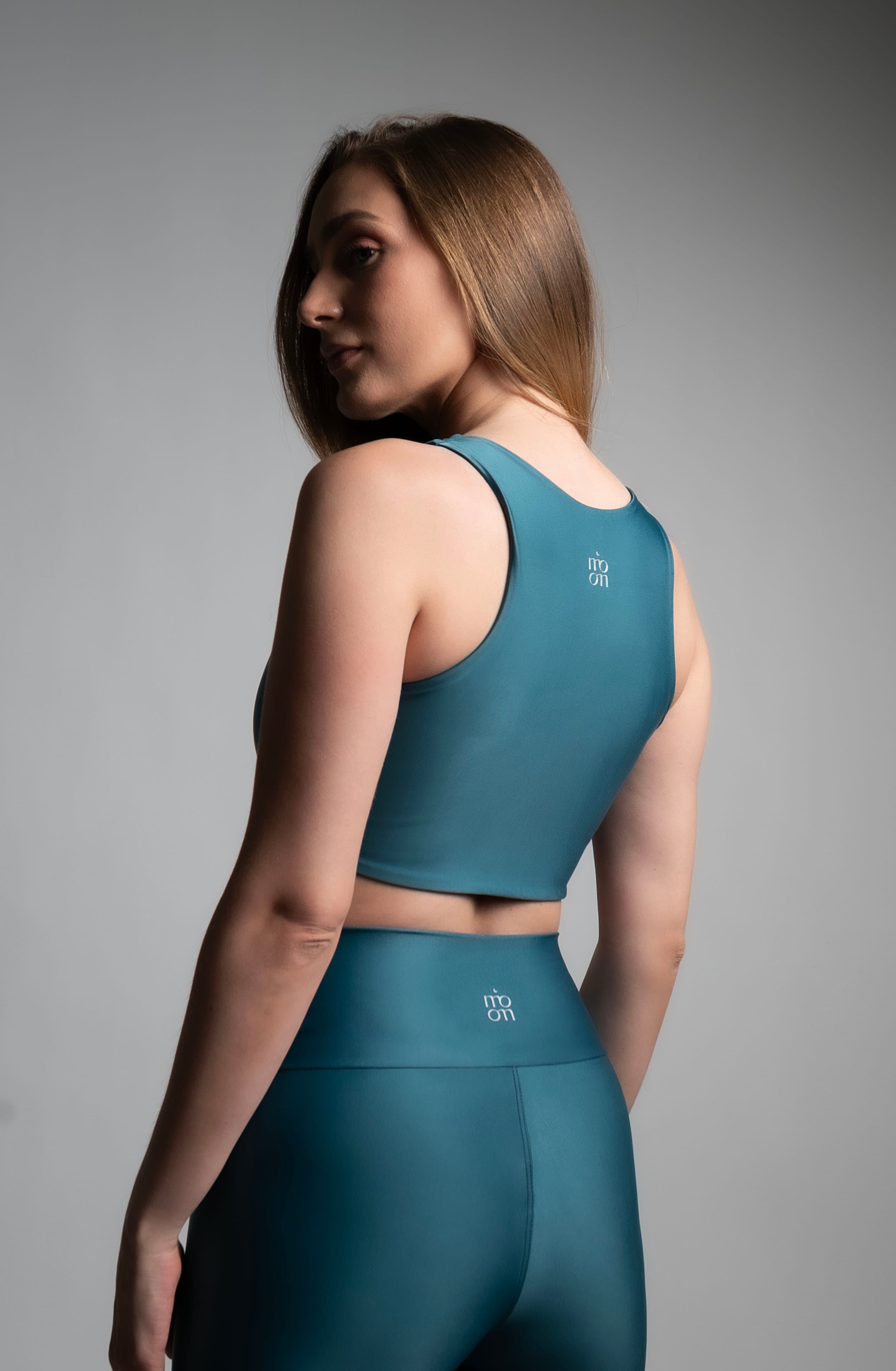 Fotografía comercial de ropa deportiva, conjunto verde azulado, vista de espalda sobre fondo de estudio