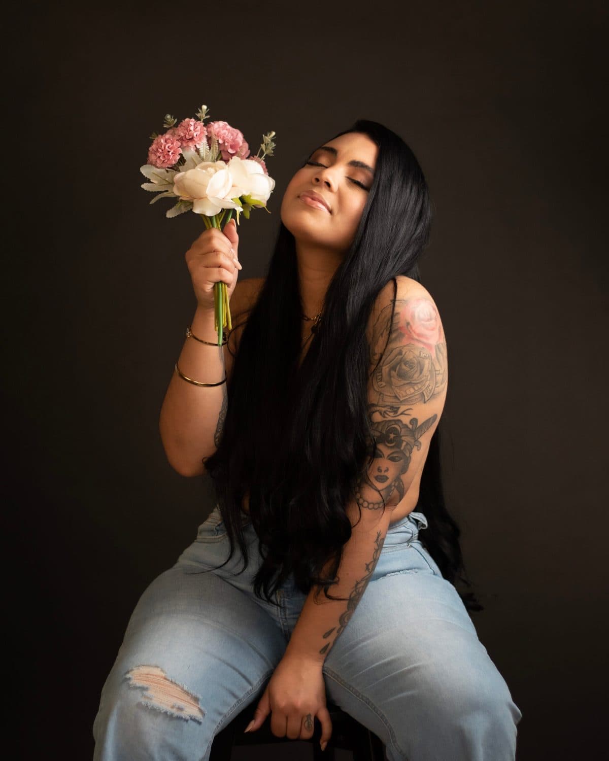 Retrato editorial con tatuajes, sosteniendo un ramo de flores, ojos cerrados sobre fondo oscuro